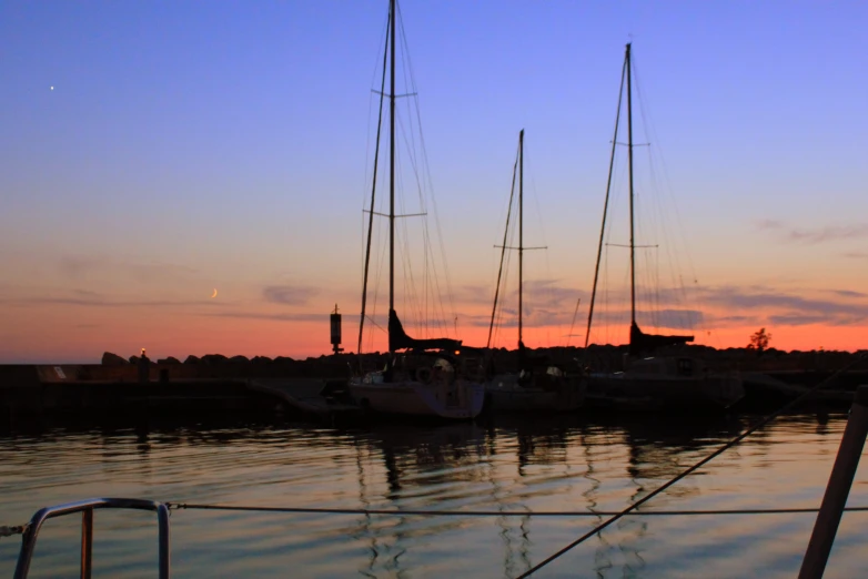 a sunset view shows the masts and sails of some sailing boats