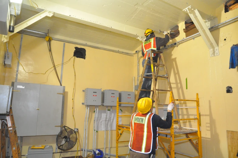 two workers on ladders working in the middle of a room