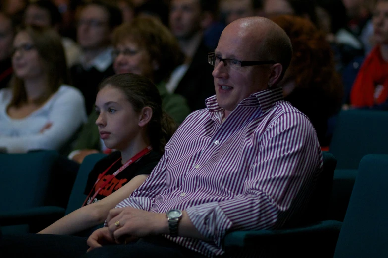 an older man with glasses sitting in the front of a crowd