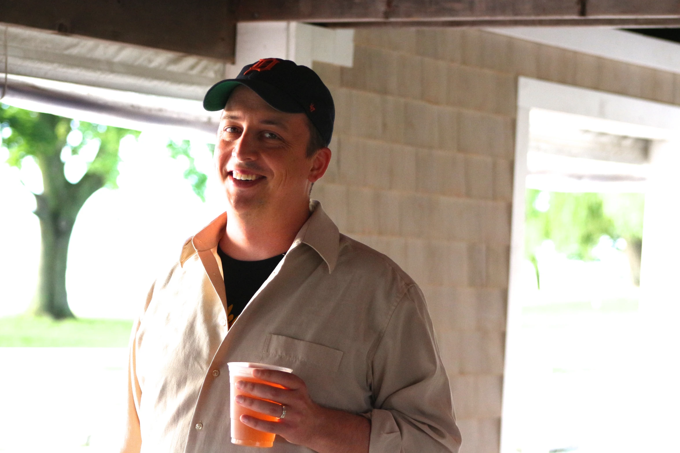 a man standing outside wearing a baseball cap and holding a coffee cup