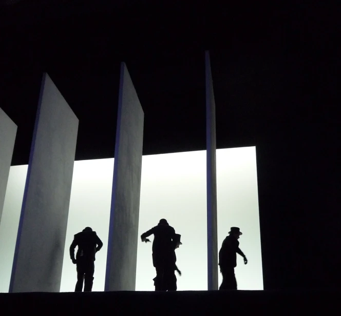 three silhouettes of people standing between two tall poles