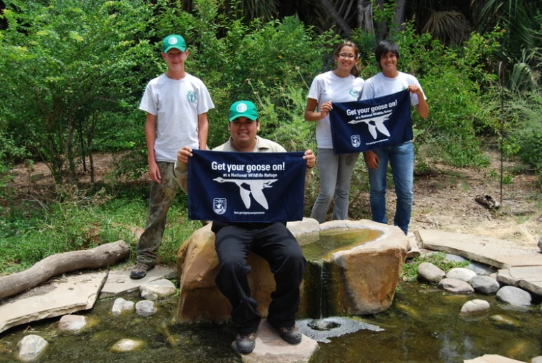 four people in blue shirts standing on rocks next to a creek