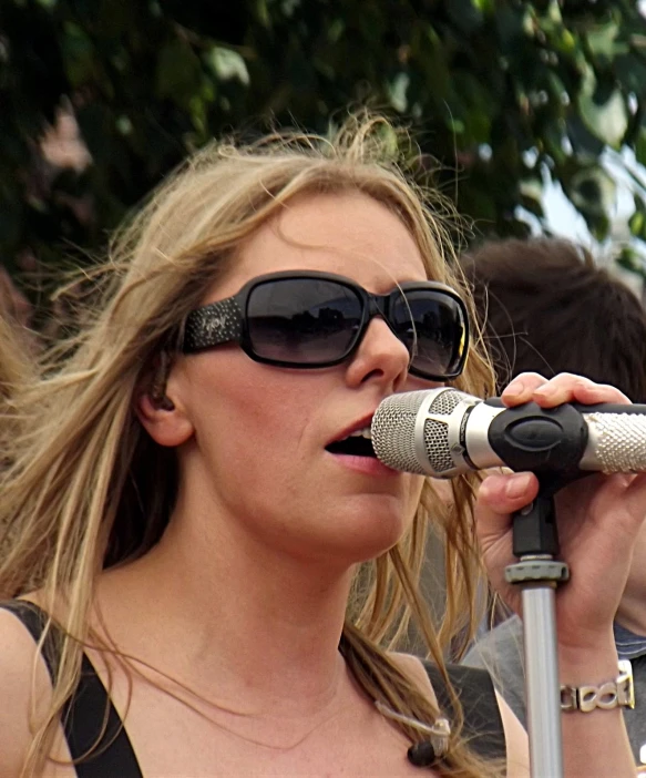 a woman wearing sunglasses while singing into a microphone