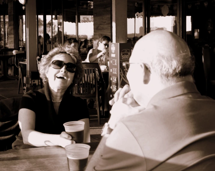 the woman sits at the table with a man as the man and the lady stare into the window