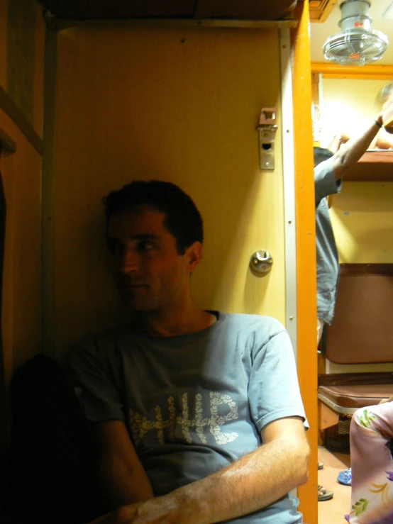 a man wearing a tee sitting in front of a wooden shelf