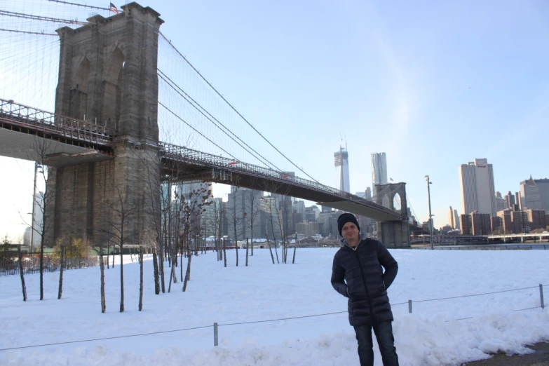 the man in winter clothing is standing under a bridge