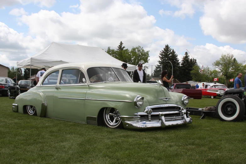 a green car is sitting on a lawn by people