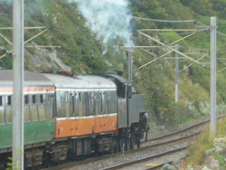 a passenger train traveling along train tracks next to green hills