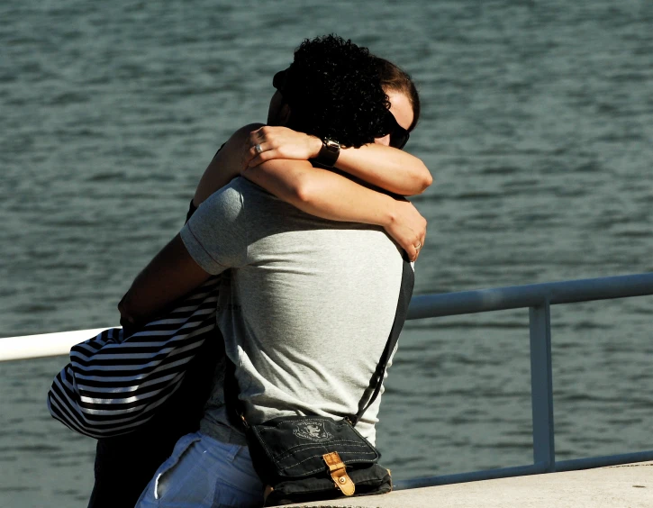 a man and woman hugging while sitting at the edge of a deck overlooking a body of water