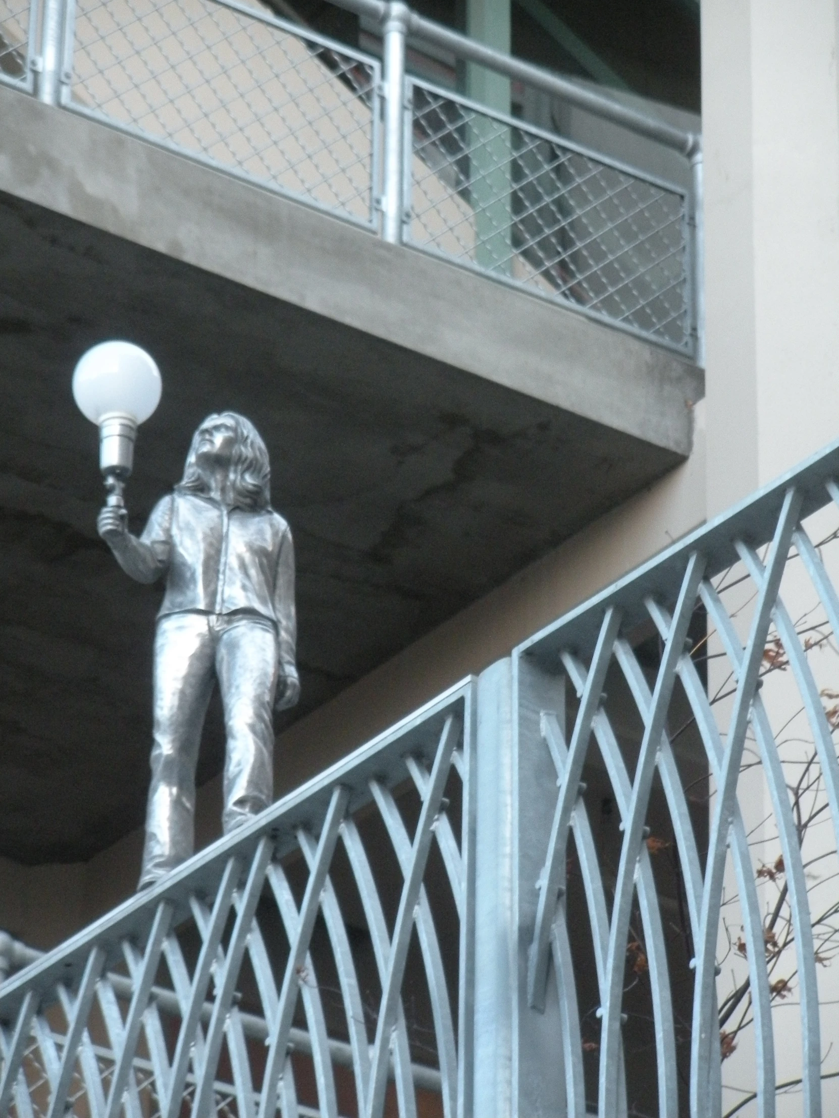 a metal statue holding a lightpost under a bridge