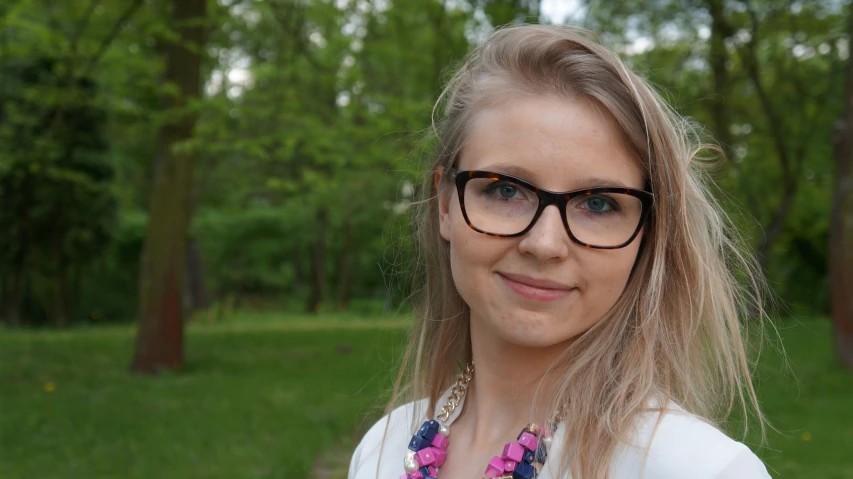 a woman in glasses with some trees in the background