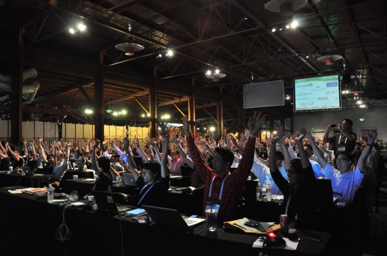 a crowded room filled with people raising their hands up