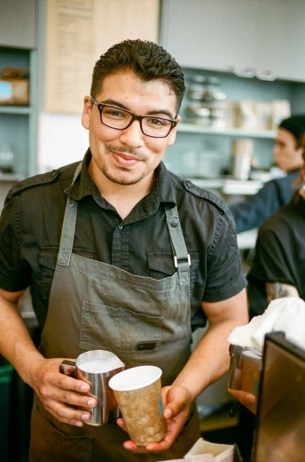 a man in an apron holding two mugs in one hand