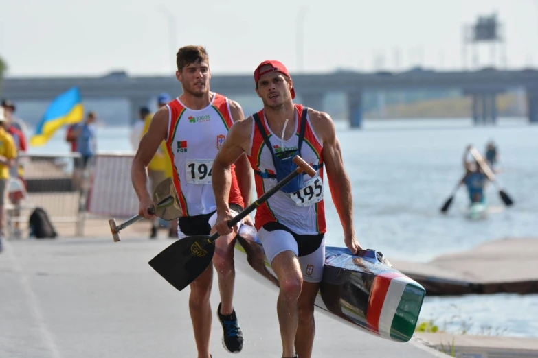 two men carry long boards down a boardwalk