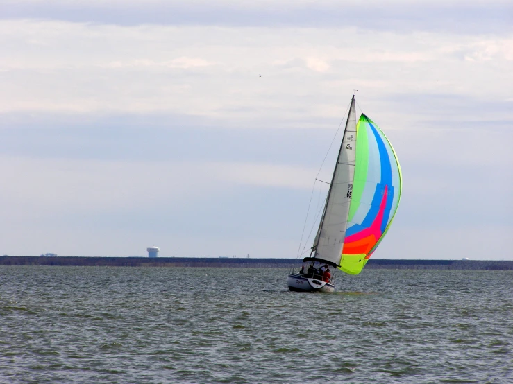 colorful sail boat on water near lighthouse on cloudy day