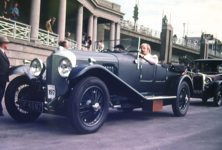 people watching people in an old car driving down the road