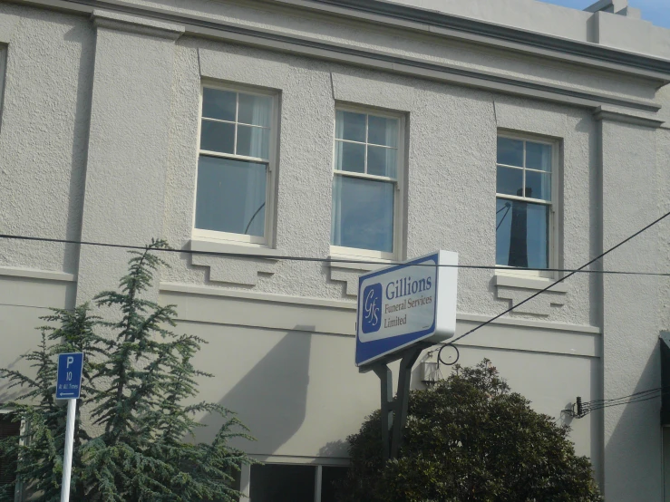 a blue and white street sign sitting below two large windows