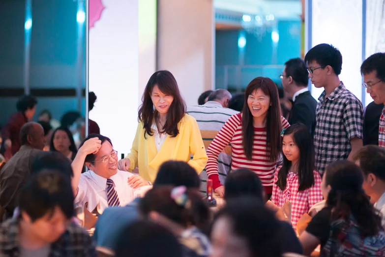 two adults are standing by tables while some people sit at the tables