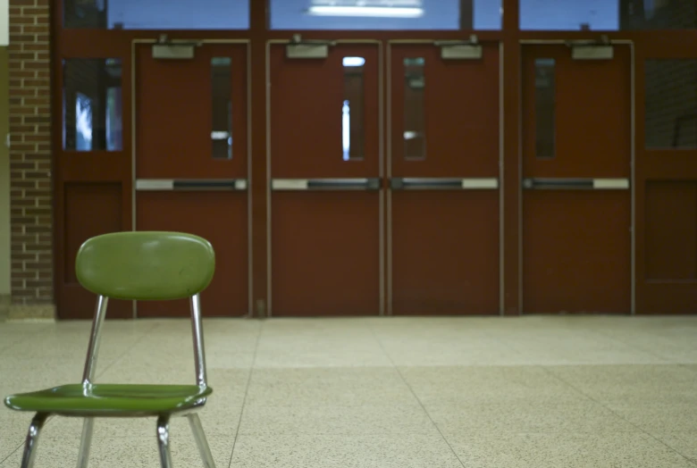 green chair outside doorway of school building with doors