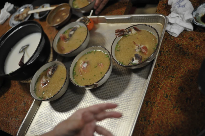 several bowls of soup and rice on a tray with a hand in front of it