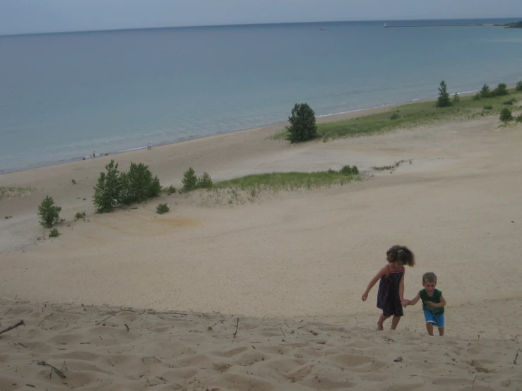 two s walking up the side of a sand dune