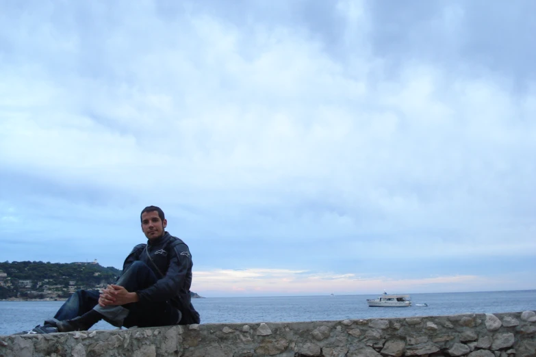 man sitting on a stone wall overlooking a boat in the water