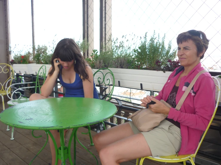 two women sitting at a table talking on cell phones