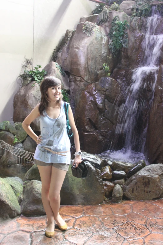 a girl standing in front of a waterfall wearing a hat