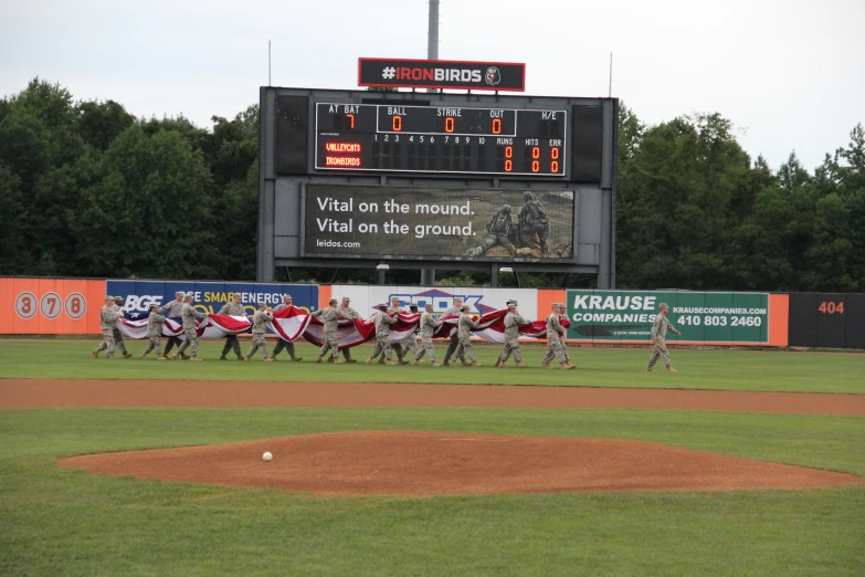 a baseball team running across the field with an score board in the background