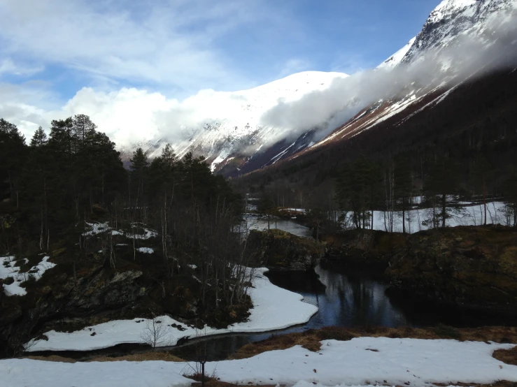 a snowy landscape near mountains with clouds and trees