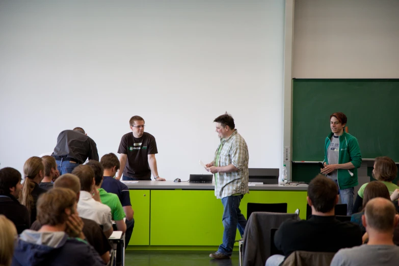 two men in front of a class of students standing and sitting