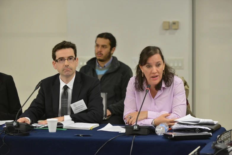 a man and woman sit at a table in front of a microphone, talking