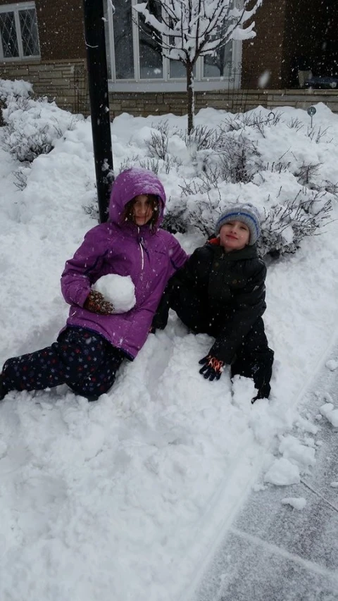 two children are sitting on snow near a lamp post