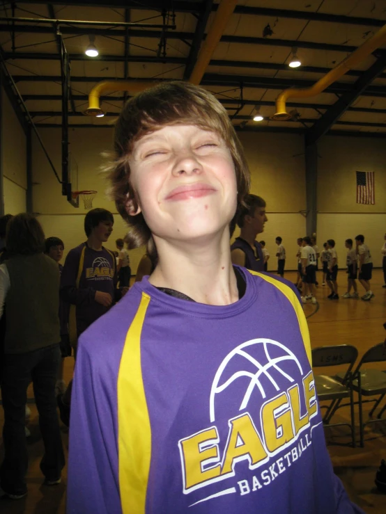 a smiling boy wearing a purple and yellow basketball uniform