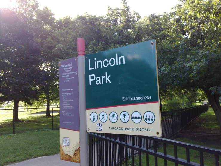 a large sign posted in the park by the fence