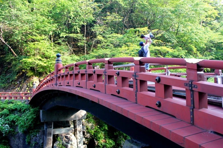 two people standing on top of a red bridge over water