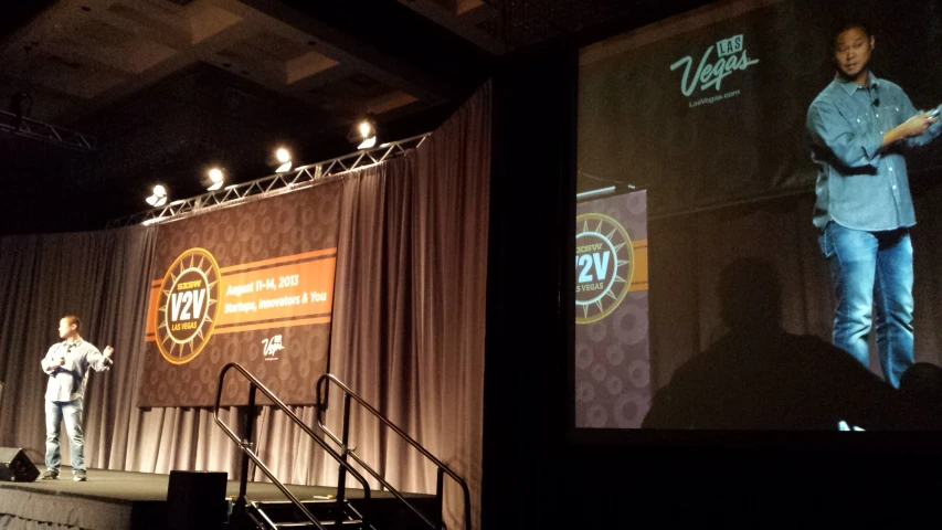 man on stage standing next to podium giving presentation