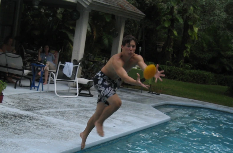 a shirtless man jumping in to a pool with an orange frisbee