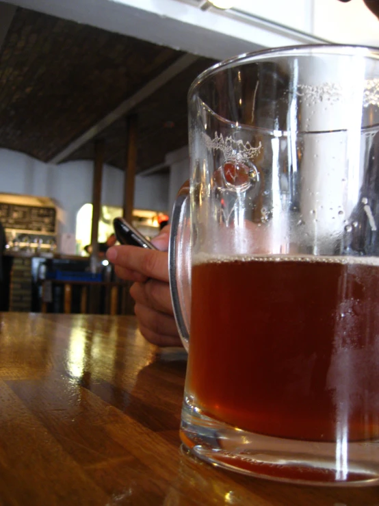 a glass mug full of liquid and a person holding a phone