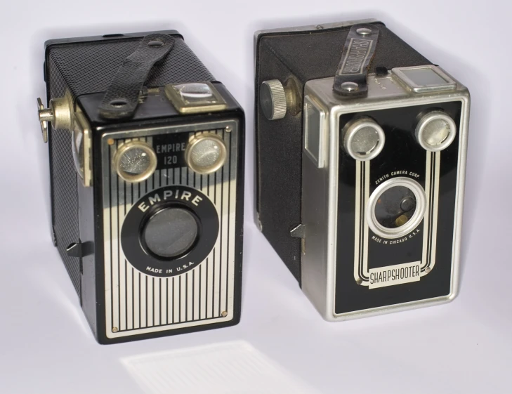 two old cameras next to each other on a white table