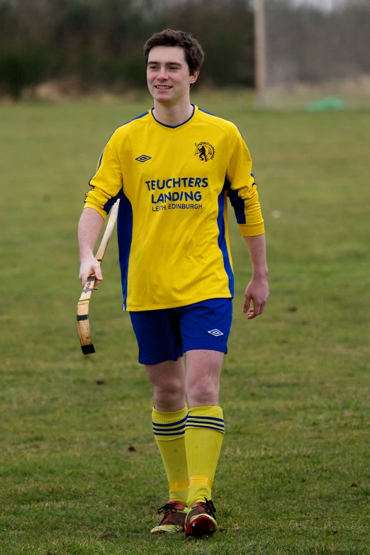 a man holding a baseball bat walking across a soccer field