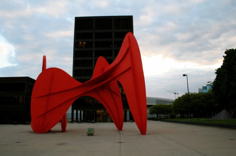 a sculpture on the corner of a parking lot with an office building in the background