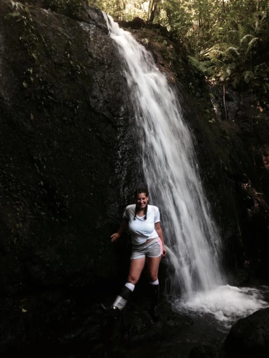 a woman standing by a waterfall with boots on