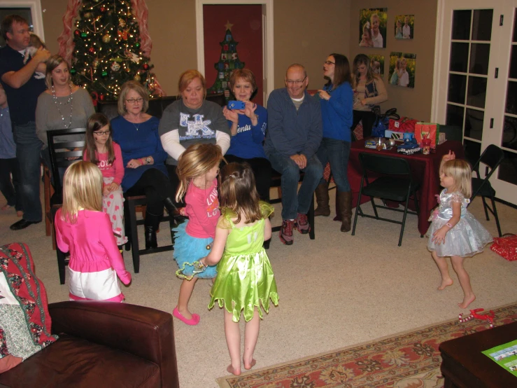 a group of people in a living room, some are holding a child and a lady is pointing