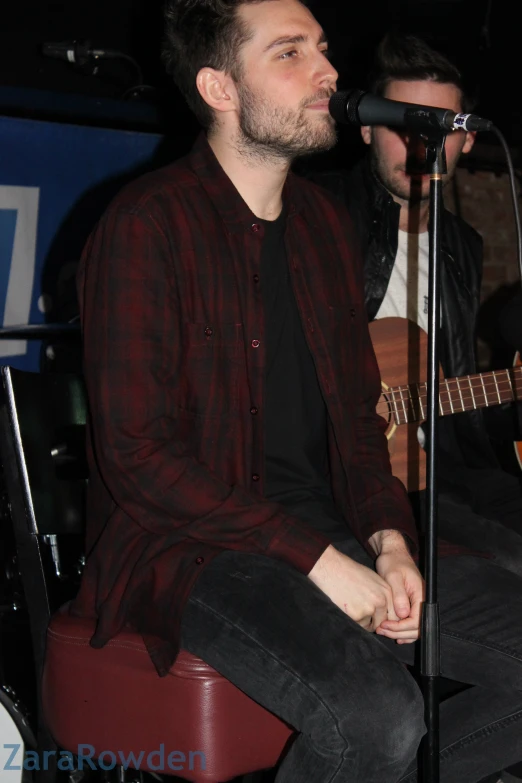 a man in a dark shirt playing guitar and singing into a microphone