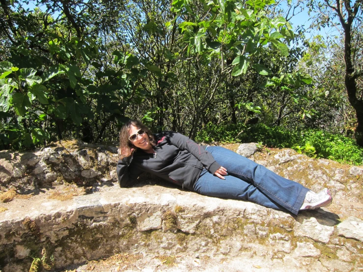 a woman with glasses laying on top of a rock next to trees