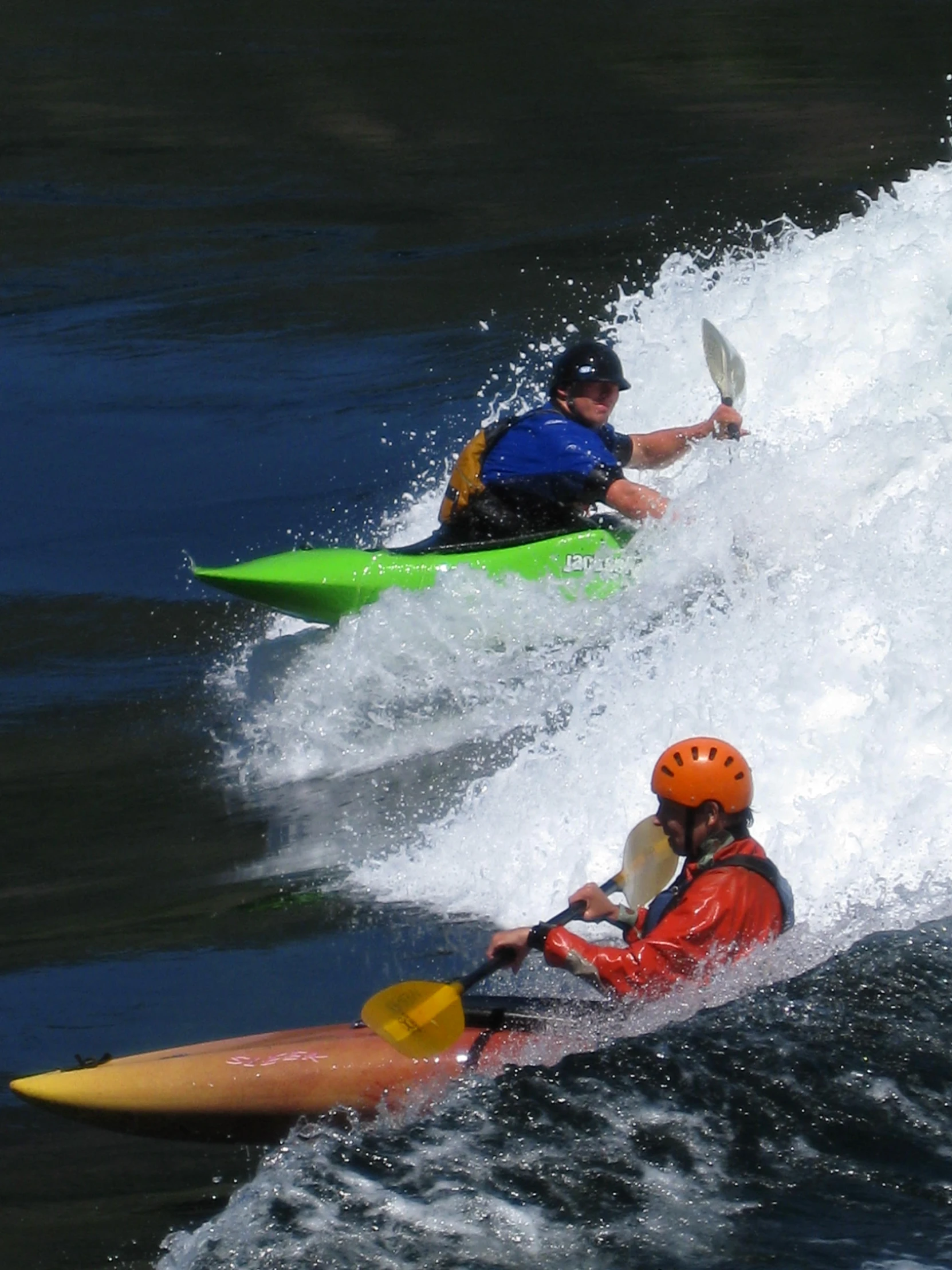 two people in their kayaks going down an ocean wave