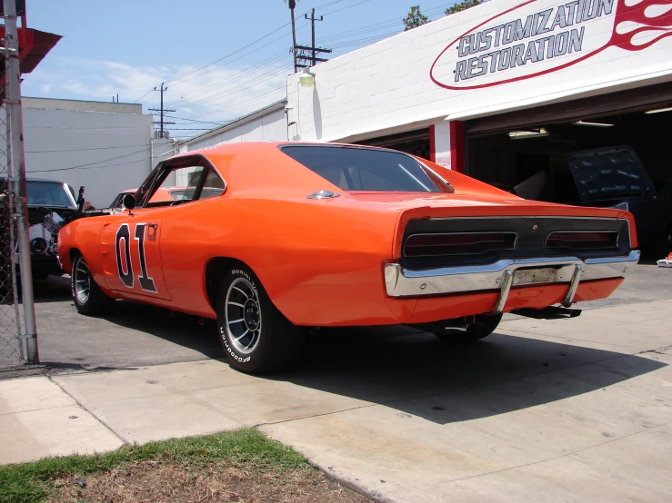 orange classic car in front of a auto shop