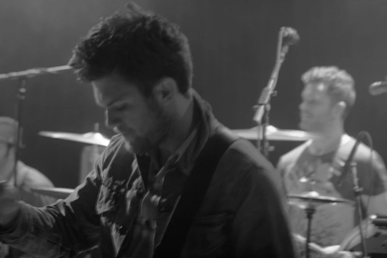 black and white image of man playing guitar with band on side