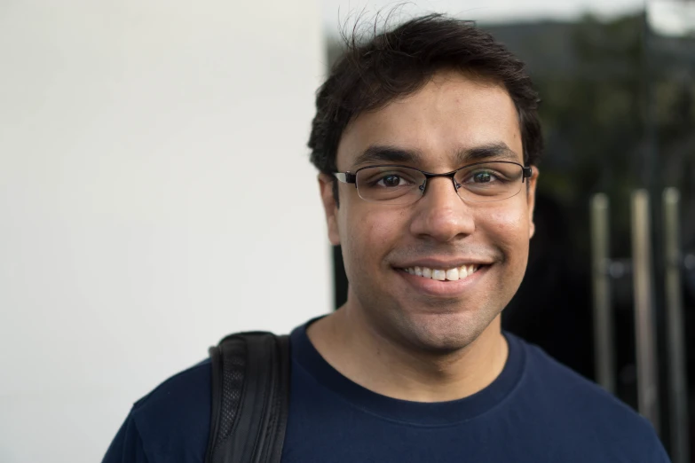 a smiling man with glasses and a backpack